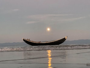 Un bote en la playa con olas y el reflejo de la luna.