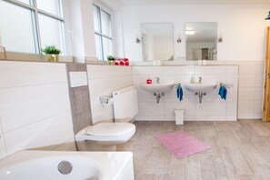 A modern bathroom with a toilet, sink, and bathtub. There are two sinks, a mirror above the sink, and a window providing natural light. - Ilsestein - Detached house (Ilsenburg)