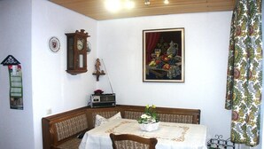 A dining area with a table set for two, a wooden bench, a wall clock, a framed picture, and a radio. - "To the dike warden" (Losheim am See)