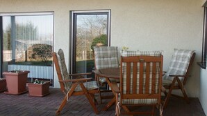 A patio with two wooden chairs and a table, large windows, and potted plants. - "To the dike warden" (Losheim am See)