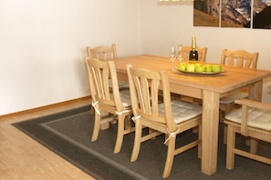 Uma mesa de jantar com seis cadeiras de madeira, uma garrafa de champanhe e um prato de maçãs.