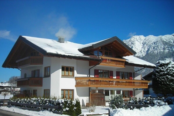 Chalé de dois andares com varanda, rodeado por neve e montanhas.