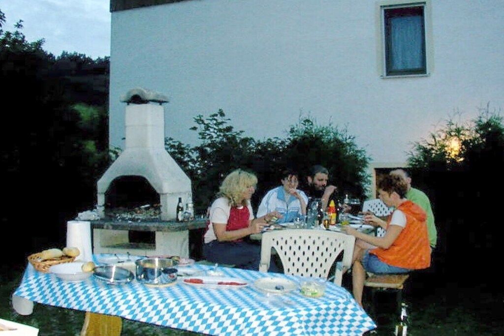Ein Essbereich im Freien mit kariertem Tischlein, einem Pizzaofen und Gästen, die an einem Tisch sitzen.