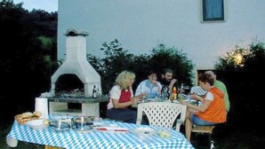 Uma área de refeições ao ar livre com toalha xadrez, um forno a pizza e hóspedes sentados à mesa.
