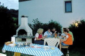 Un'area pranzo all'aperto con tovaglia a scacchi, un forno per pizza e ospiti seduti a tavola.