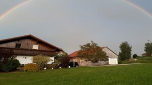 Paisagem rural com duas casas, um campo gramado e um arco-íris no céu.