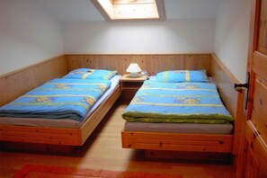 Una stanza piccola con due letti di legno, ognuno con copriletto a motivi blu e gialli, un comodino con una lampada e un lucernario sopra.