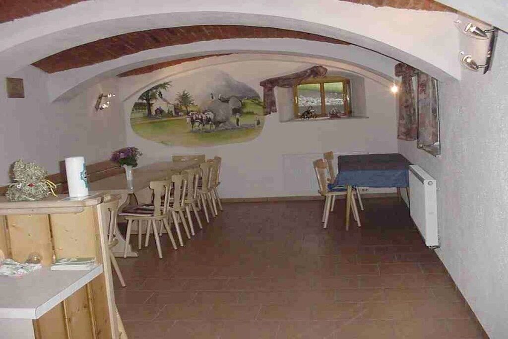 A dining area with a mural, wooden furniture, and a view through an archway.