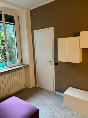 A room with a window, a door, a radiator, a purple bench, and a cabinet.