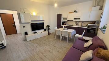 Un soggiorno moderno con televisione a schermo piatto, un divano e un'area pranzo con sedie.