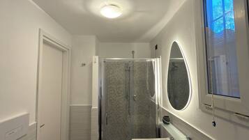 Un bagno moderno con cabina doccia in vetro, lavabo bianco e specchio con riflessi azzurri.