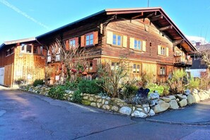 A wooden chalet with multiple windows and balconies, surrounded by a stone wall and vegetation. - Alpenflair holiday apartment 316 (Oberstdorf)