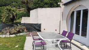 Een terras buiten met een tafel en stoelen, omringd door een witte muur en een glazen deur.
