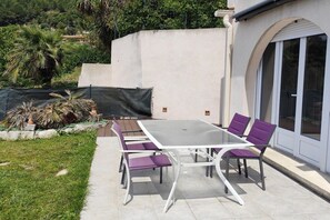 An outdoor patio with a table and chairs, surrounded by a white wall and a glass door. - Holiday apartment in Èze with swimming pool (Èze)