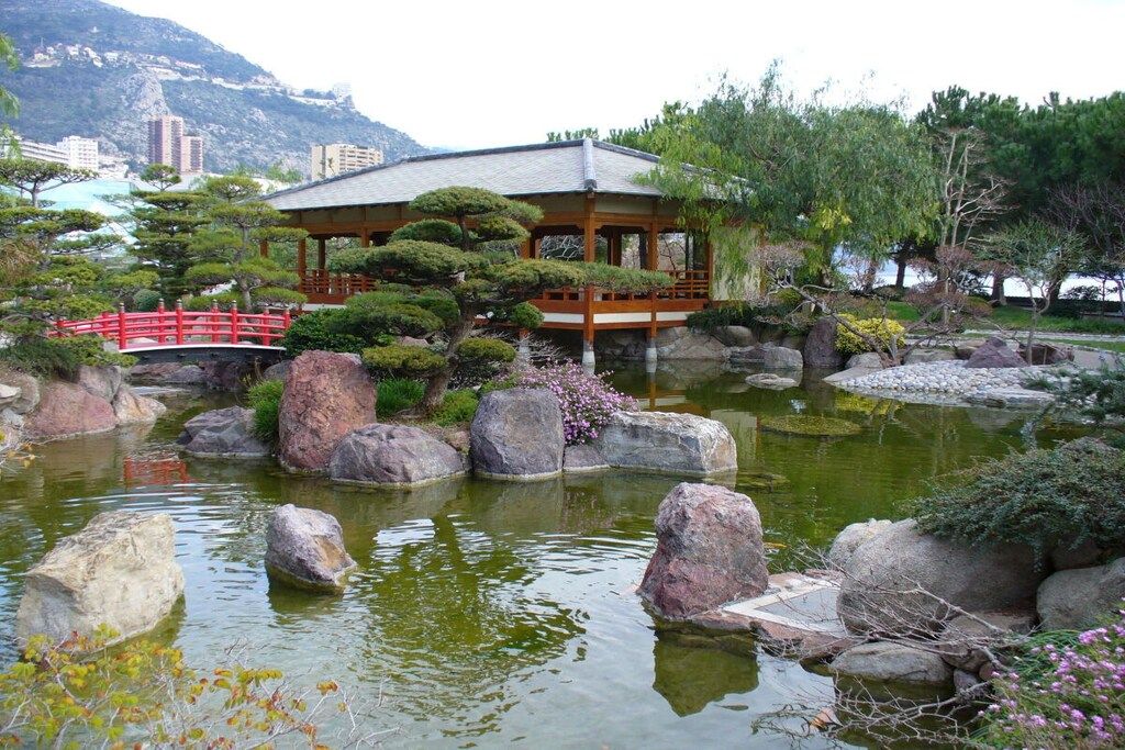 Un tradizionale padiglione giapponese con un giardino, che include uno stagno con rocce e un ponte rosso.
