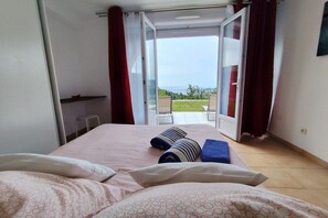 A bedroom with a bed, pillows, a blue towel, and a view of a balcony with chairs. - Holiday apartment in Èze with swimming pool (Èze)