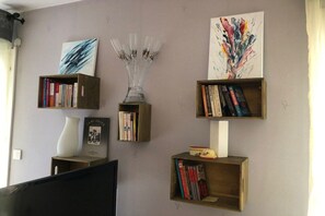 A room with a flat-screen TV, two wooden bookshelves with books, a vase, and two abstract paintings. - Holiday apartment with 1 bedroom (Colmar)