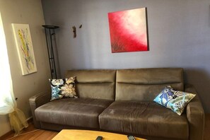 Ein braunes Ledersofa mit floralen Kissen, ein rotes abstraktes Gemälde und eine Stehlampe.