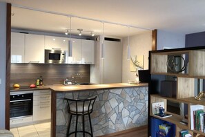 Eine moderne Küche mit Steinrückwand, Edelstahlgeräten und einer Bar mit Hockern.
