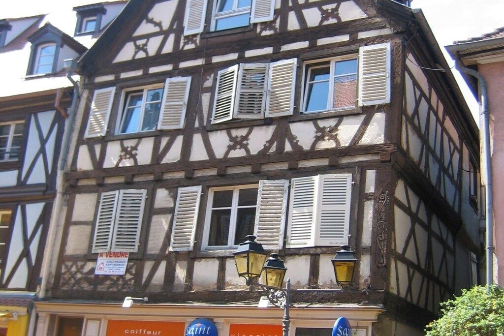 A traditional half-timbered building with multiple windows, some with shutters, and a sign indicating a sale.