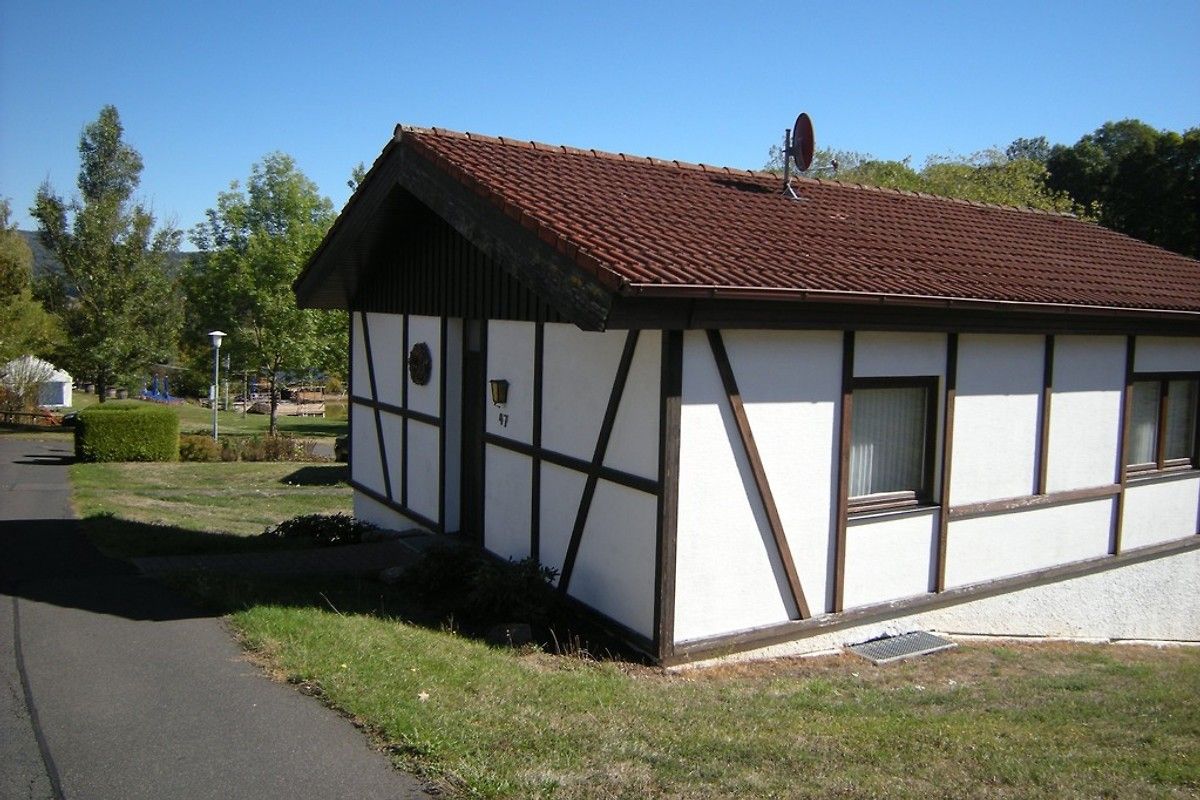 Ein kleines, eingeschossiges Gebäude mit geneigtem Dach, weißen Wänden und schwarzem Zierstreifen sowie einer kleinen Veranda.