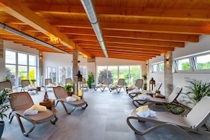 A sunlit indoor relaxation area with lounge chairs, potted plants, and a view of the outdoors.