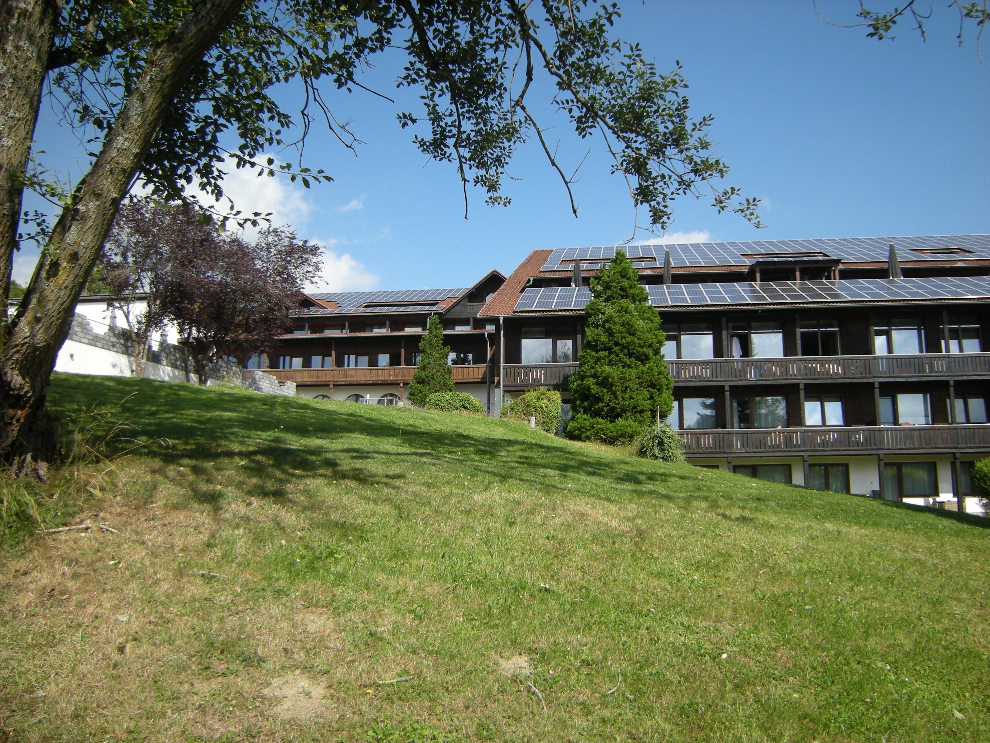 A building with multiple balconies, solar panels on the roof, and a grassy slope.