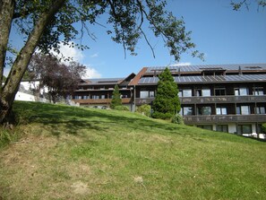 A building with multiple balconies, solar panels on the roof, and a grassy slope.