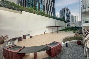 Um terraço no telhado com área de churrasco, espaço para sentar e vista dos edifícios ao redor.