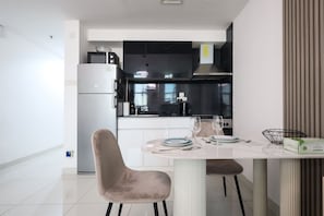 Cozinha moderna com área de refeições, destacando uma geladeira branca, armários pretos e uma mesa posta para dois.