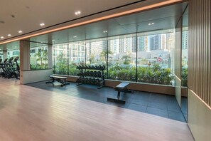 A gym with exercise equipment, a bench, and a view of a cityscape through large windows. - Stylish JVC Studio at Binghatti Aurora, Dubai (Dubai)