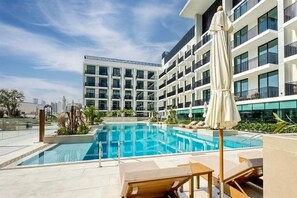 A modern hotel with a rooftop pool, sun loungers, and a view of the city skyline. - Stylish JVC Studio at Binghatti Aurora, Dubai (Dubai)