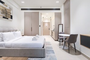 Habitación de hotel moderna con una cama grande, un escritorio y una silla. Se observa un armario y un baño al fondo.