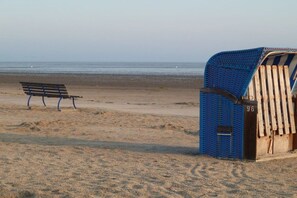 Ein Strand mit einer Holzbank und einer blau-weiß gestreiften Strandhütte.