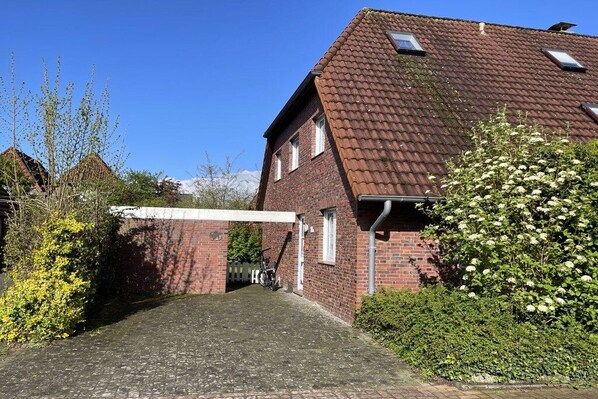 Ein Wohngebäude mit Backsteinfassade, Ziegeldach und einer gepflasterten Auffahrt zu einem verschlossenen Eingang.