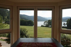 Ein Zimmer mit Blick auf einen See und Berge durch große Fenster.
