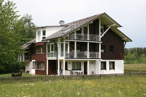 Ein zweistöckiges Haus mit Balkon, Satellitenschüssel und umzäunter Garten.