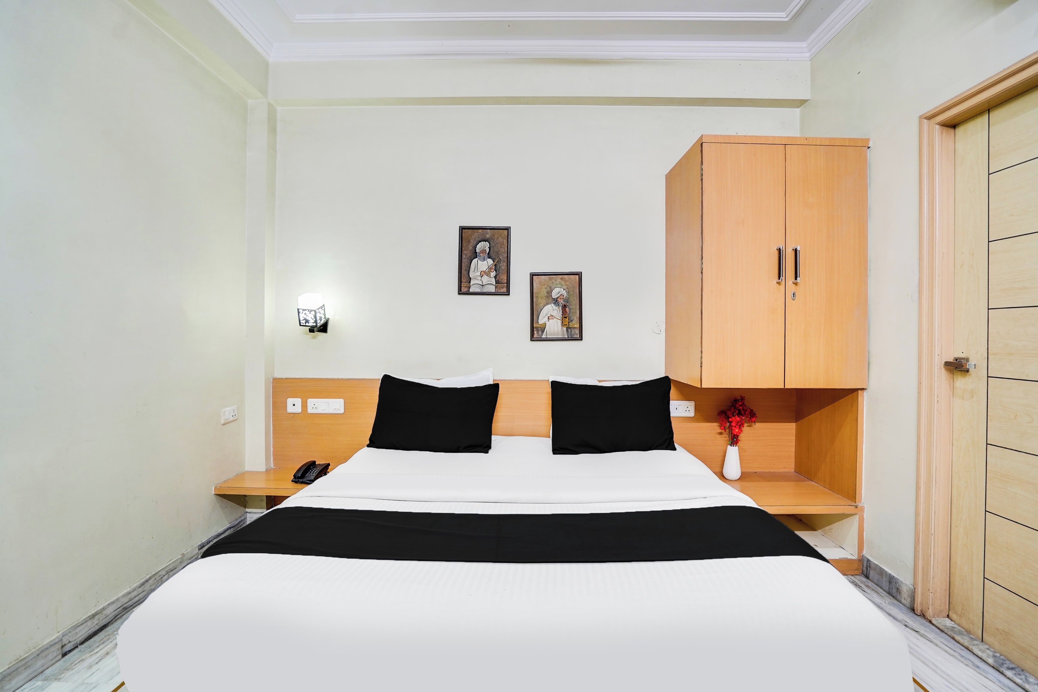 A hotel room with a bed, bedside tables, a wardrobe, and two framed pictures on the wall.