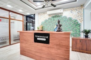 En receptionsdisk med et 'Townhouse'-skilt, en loftsvifte og et dekorativt påfugl-maleri.