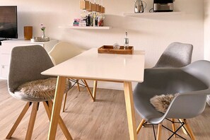 Uma sala de jantar moderna com uma mesa branca, cadeiras cinzas e chão de madeira.