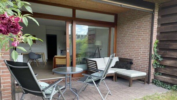 Eine Außenpatio mit Esstisch und Stühlen, einer Sitzecke und einer Glastür, die in einen Innenraum führt.