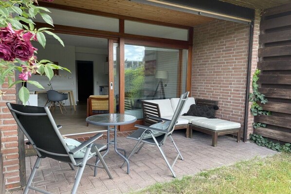 Um pátio externo com mesa e cadeiras de jantar, um sofá e uma porta de vidro deslizante que dá para um espaço interno.