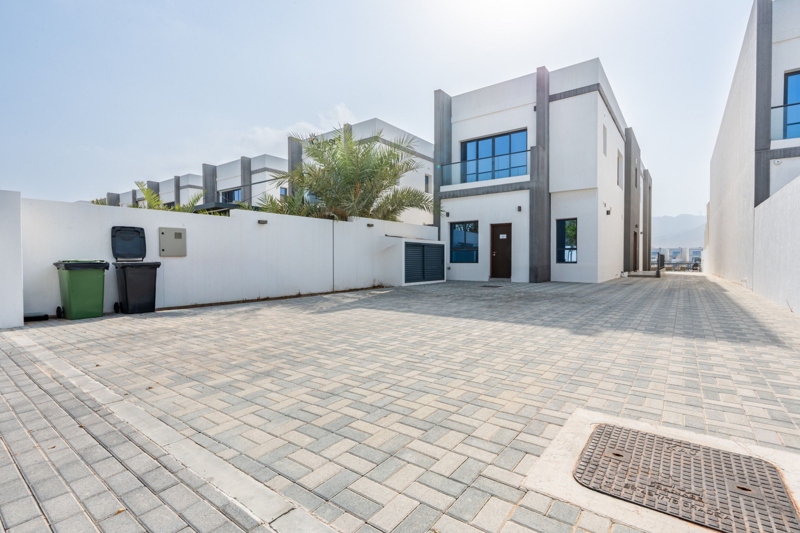 A modern building with a paved courtyard, a green trash bin, and a metal grate.