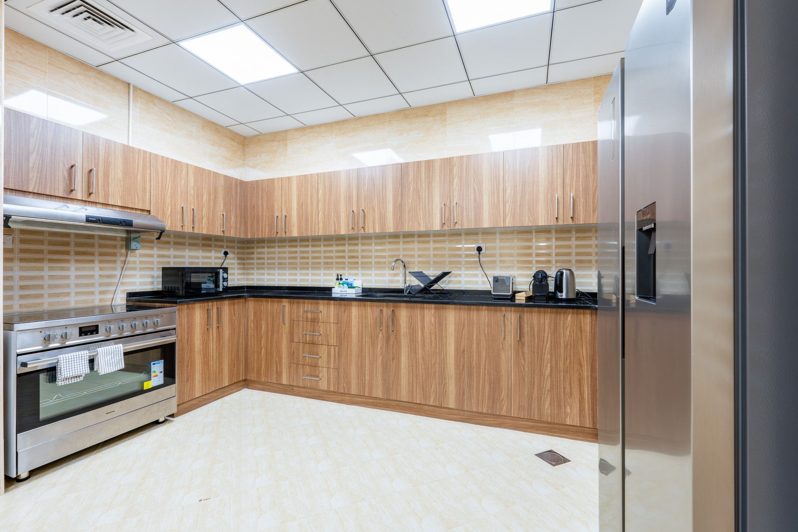 A modern kitchen with wooden cabinets, a stainless steel refrigerator, a built-in oven, and a microwave.