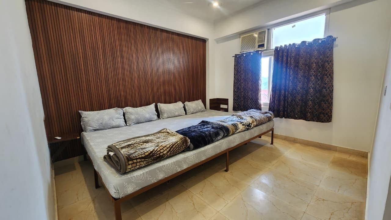 A bedroom with a bed, a wooden headboard, a window with curtains, and a tiled floor.