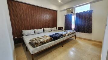 A bedroom with a bed, a wooden headboard, a window with curtains, and a tiled floor.