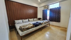 A bedroom with a bed, a wooden headboard, a window with curtains, and a tiled floor. - Brahmanchal View (Barsana)