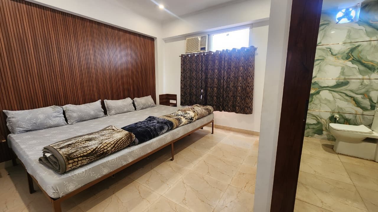 Une chambre à coucher avec un grand lit, une tête de lit en bois, une fenêtre avec des rideaux et une salle de bain avec un mur en marbre et des toilettes.