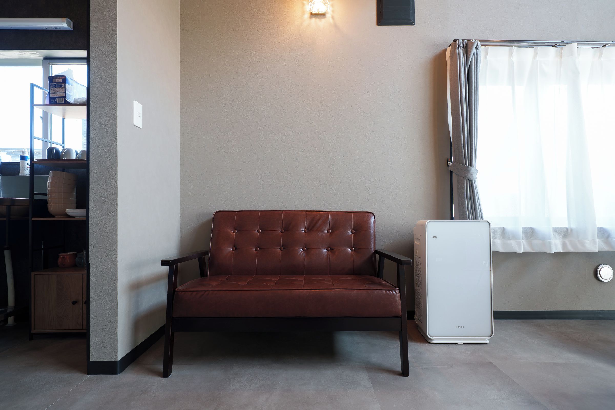 Quarto com sofá de couro marrom, radiador branco e janela com cortinas.
