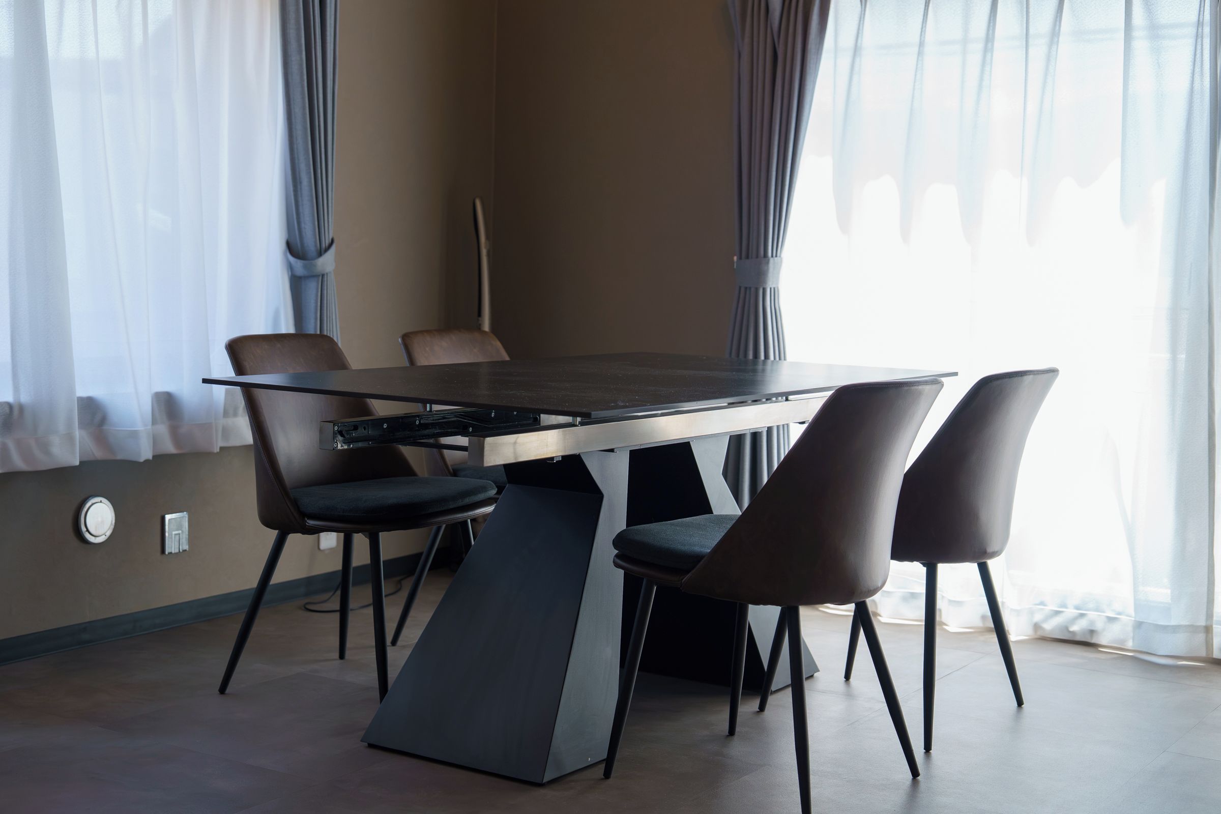Uma sala de conferências moderna com mesa de vidro, quatro cadeiras e uma grande janela com cortinas.